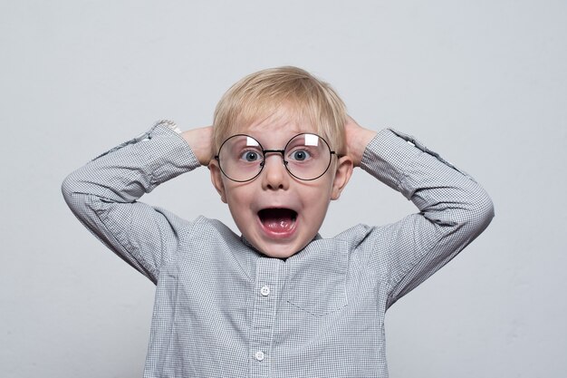 Cheerful blond boy in glasses holding hands behind his head. Half-length portrait on white background.