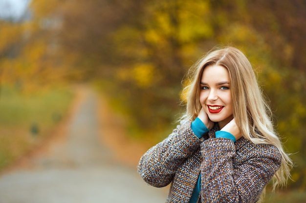 Cheerful blonde woman with red lips enjoying weather in autumn park