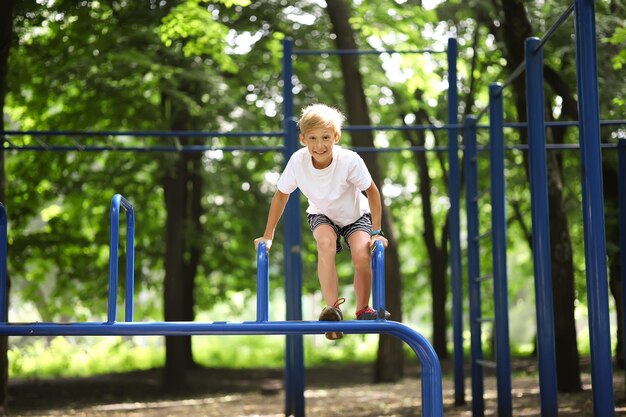 Cheerful boy athlete in the park climbed on sports equipment and laughs merrily