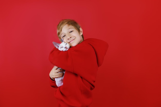 A cheerful boy in a red tracksuit hugs a little kitten and cuddles him