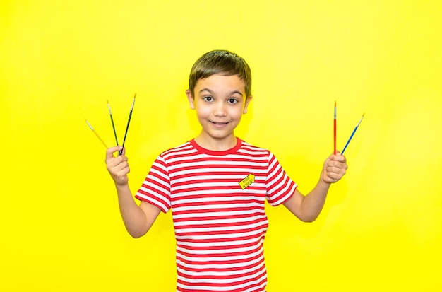 Cheerful boy in a striped tshirt holds colorful brushes in his hands