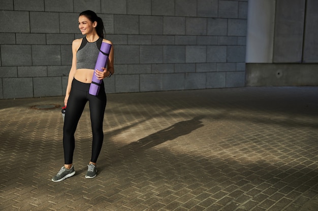 Cheerful brunette female person keeping smile on her face while going to have physical training