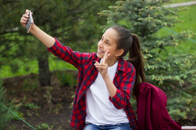 cheerful brunette girl makes a selfie on a mobile phone and shows the victory sign