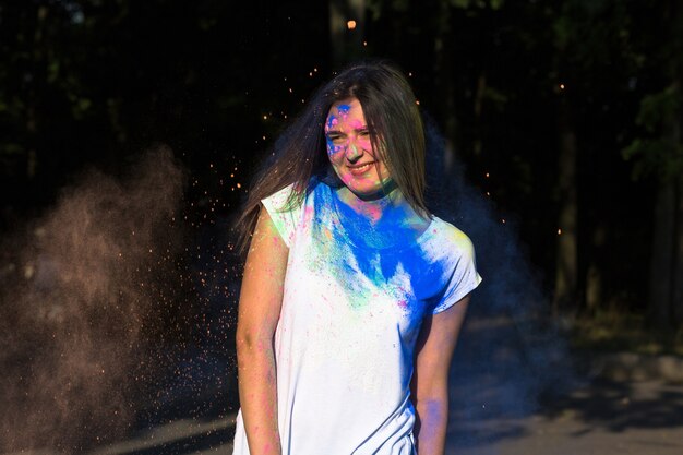 Photo cheerful brunette girl posing with exploding gulal powder in the park