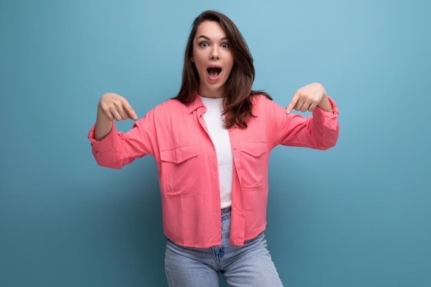 Cheerful brunette lady in a pink shirt and jeans points her finger at the infomation on a studio