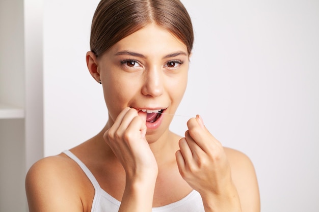 Cheerful brunette woman using dental floss in bathroom