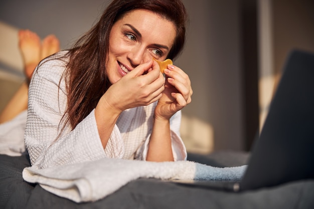 Cheerful brunette woman watching beauty tutorials online