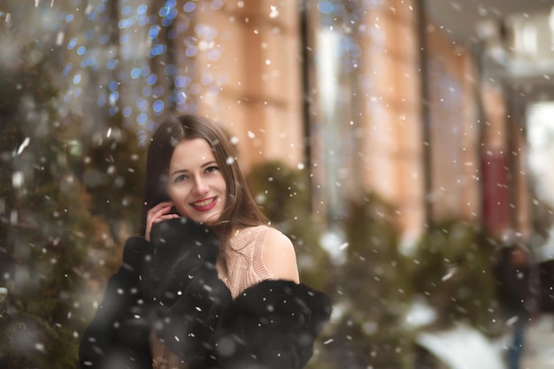 Cheerful brunette woman with bare shoulders posing near the Christmas showcase decoration with garlands. Space for text