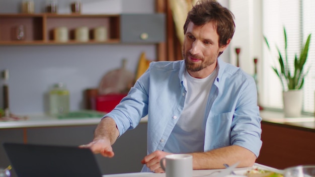 Cheerful businessman call video chat on laptop computer at remote workplace Happy man gesturing with hands on kitchen Freelancer making video chat online on laptop computer at home office