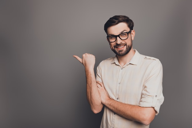 Cheerful businessman in glasses pointing away on gray