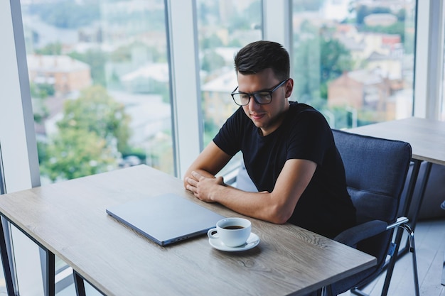 Cheerful businessman in glasses sits at his desk working with a laptop in the office A businessman sits and works on a laptop computer and drinks coffee Starting the day at the office