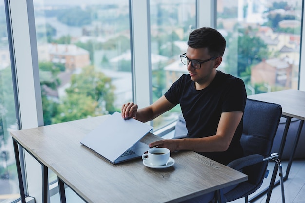 Cheerful businessman in glasses sits at his desk working with a laptop in the office A businessman sits and works on a laptop computer and drinks coffee Starting the day at the office