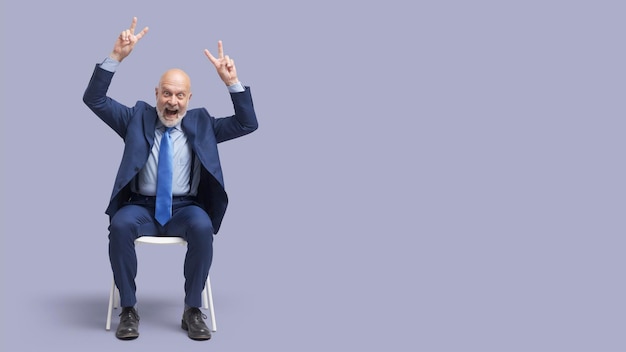 Cheerful businessman sitting on a chair and making V signs he is celebrating his success