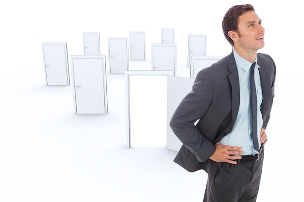 Cheerful businessman standing with hands on hips against many doors with one opening