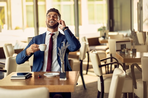 Cheerful businessman talking on the phone while having coffee break in a cafe