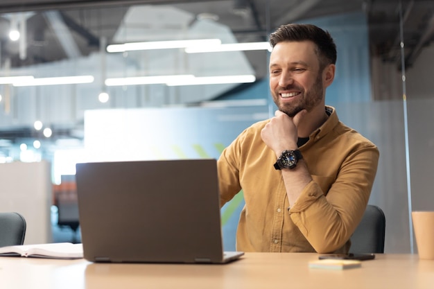 Cheerful businessman using laptop working online in office