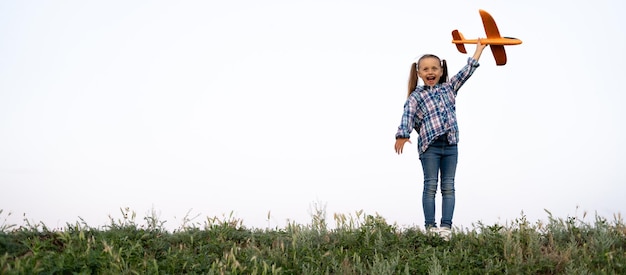 Cheerful carefree caucasian girl standing on the background of the sunset launching a toy plane into the sky happy child plays and walks in nature Active childhood concept Banner