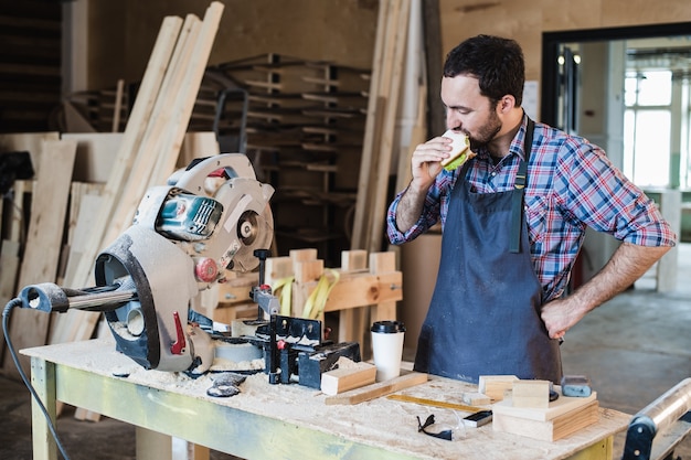 Cheerful carpentry worker having lunch eating sandwich in a workshop