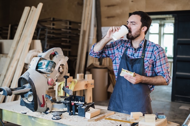 Cheerful carpentry worker having lunch eating sandwich in a workshop