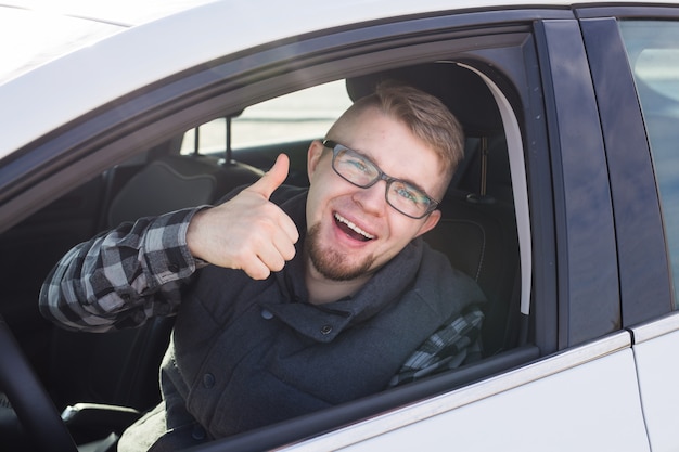 Cheerful casual guy smiling happily showing thumbs up sitting in a big white car