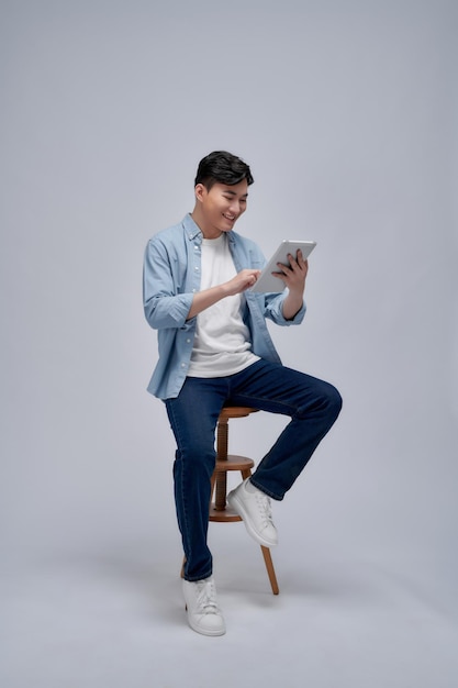 Cheerful casual man holding his tablet and celebrating with his fist in the air while sitting on a chair