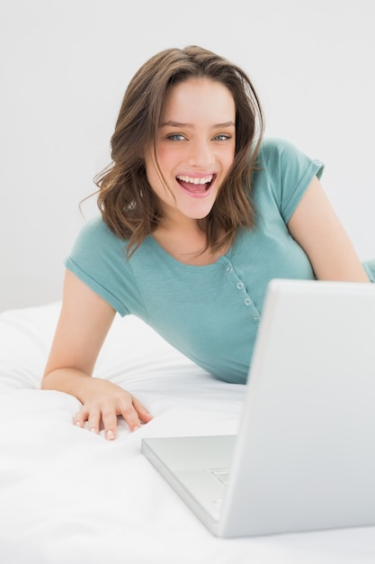 Cheerful casual woman with laptop in bed