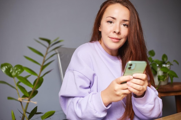 Cheerful caucasian female use her smartphone A lot of green plants around Red hair woman in violet sweater