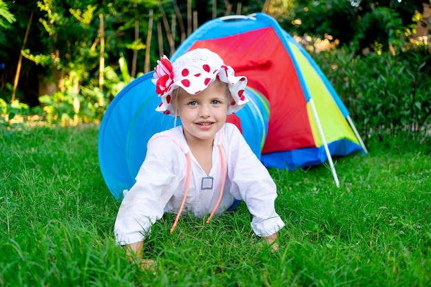 A cheerful child girl plays on the playground or in the yard of the house on the green grass in summer and laughs