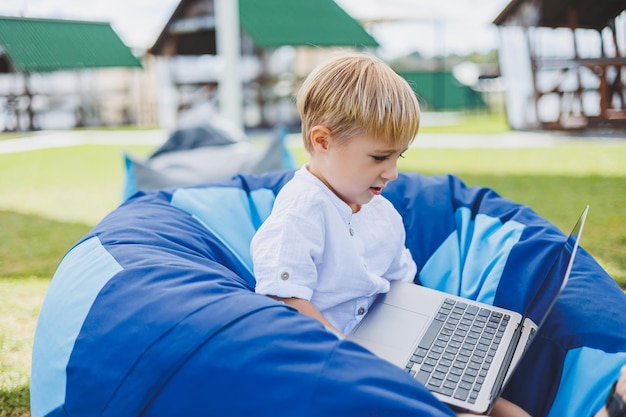 A cheerful child is playing on colorful beanbag chairs on the street A little boy watches cartoons on a laptop while sitting on a chair in the park