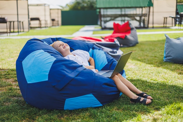 A cheerful child is playing on colorful beanbag chairs on the street A little boy watches cartoons on a laptop while sitting on a chair in the park