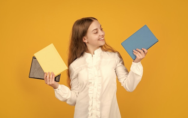 Cheerful child showing school book on yellow background back to school