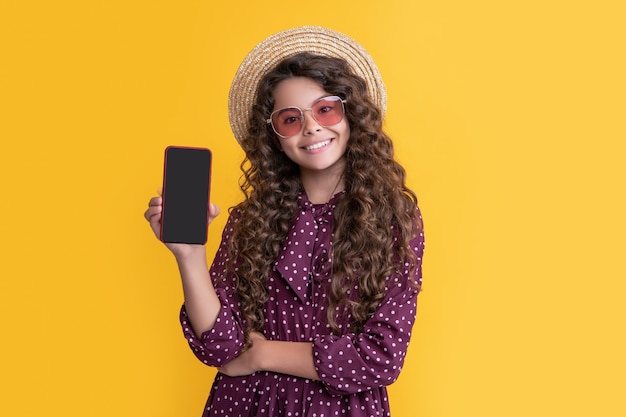 Cheerful child with curly hair presenting screen of smartphone with copy space