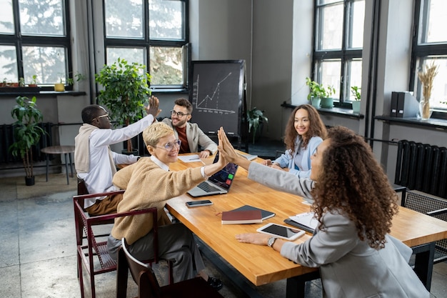 Cheerful colleagues giving one another high five over table in office