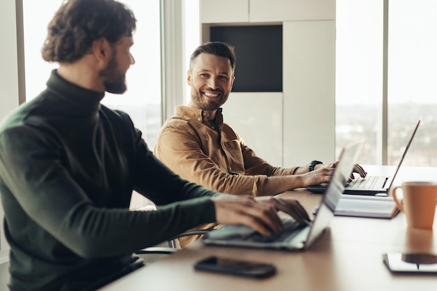 Cheerful company employees cooperating working on common business project using laptops at workplace