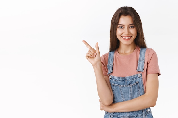 Cheerful, confident stylish modern woman in dungarees, t-shirt pointing upper left corner, laughing and smiling carefree as give hint where buy clothes during black friday, white background