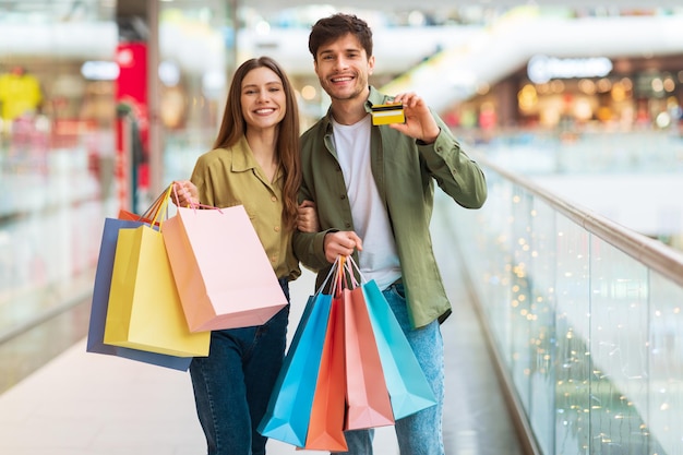 Cheerful couple showing credit card shopping in modern hypermarket