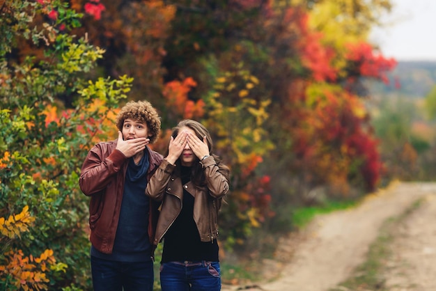 Cheerful couple shows emotions man and woman in leather jackets and jeans show surprise against background of autumn trees