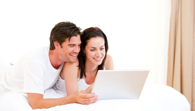 Cheerful couple using a computer lying on their bed 