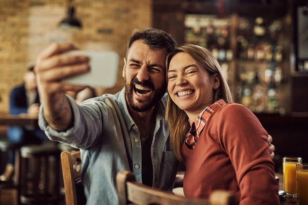 Cheerful couple using smart phone and taking selfie in a cafe