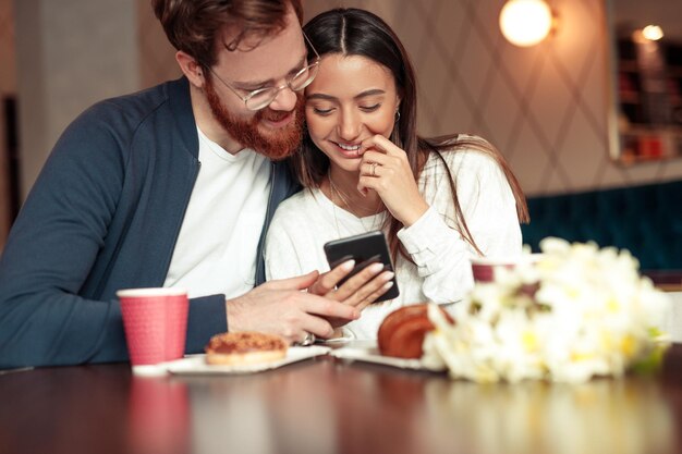 Photo cheerful couple using smartphone in cafe