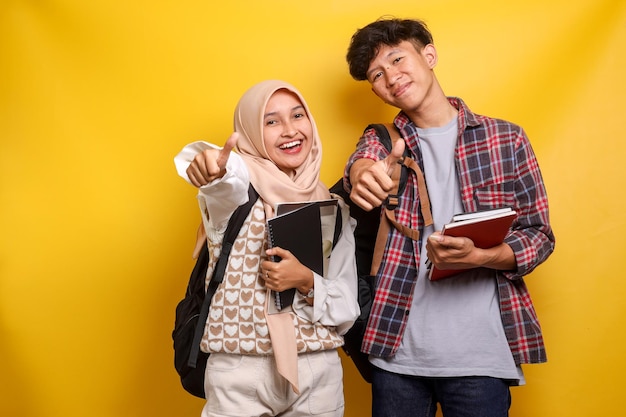 Cheerful couple of young man and woman in hijab wearing casual clothes and backpack showing thumbs u