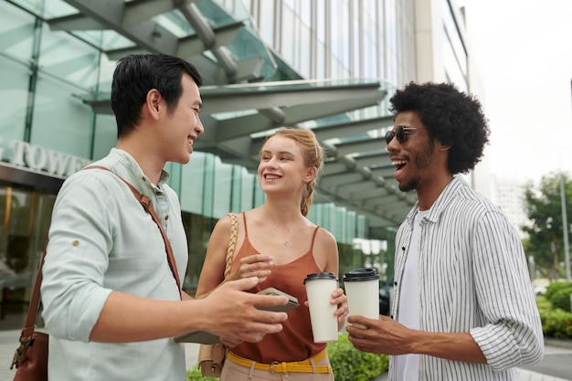 Photo cheerful coworkers standing out office building drinking coffee and discussing news