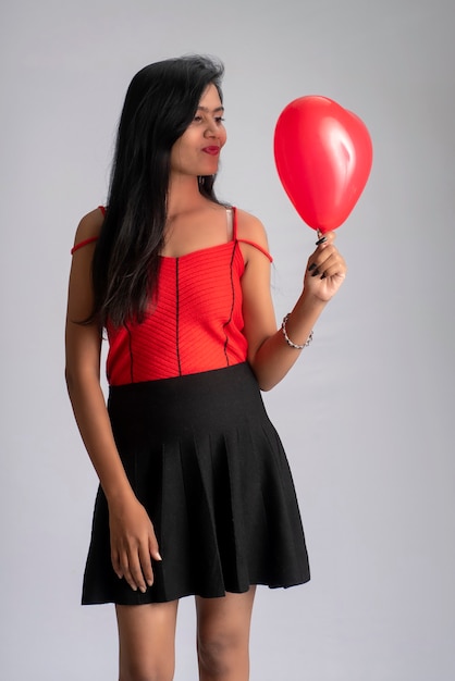 Cheerful cute girl in fancy red and black outfit posing with heart shape balloon.