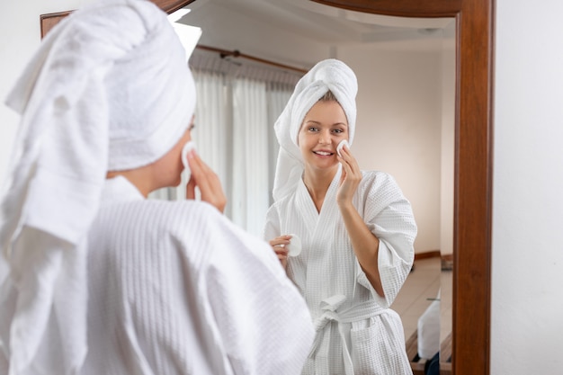 Cheerful cute woman in a white waffle bathrobe with a towel on her head