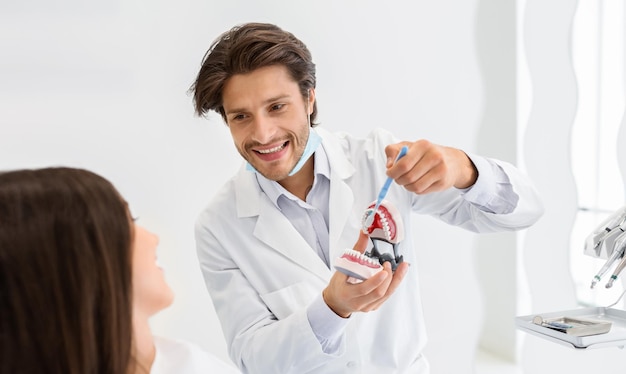 Photo cheerful doctor showing how to brush teeth using jaw model