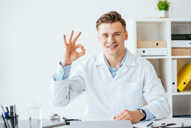 Cheerful doctor in white coat showing ok sign in clinic