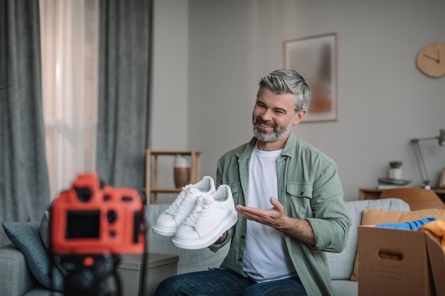 Cheerful elderly european man blogger with beard records video review on shoes unpacks purchases