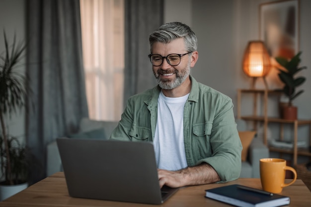 Cheerful elderly european man with beard in glasses watches video lesson chatting on computer