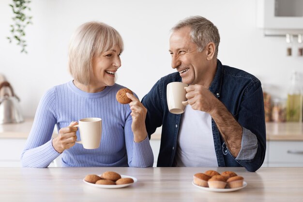 Cheerful elderly man and woman drinking tea at home