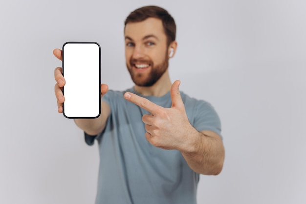 Cheerful Emotional Bearded Man Holding Blank Cell Phone In Hand Showing White Screen To Camera Pointing At You Happy Millennial Guy Recommending New Application Or Mobile Website Mockup Banner